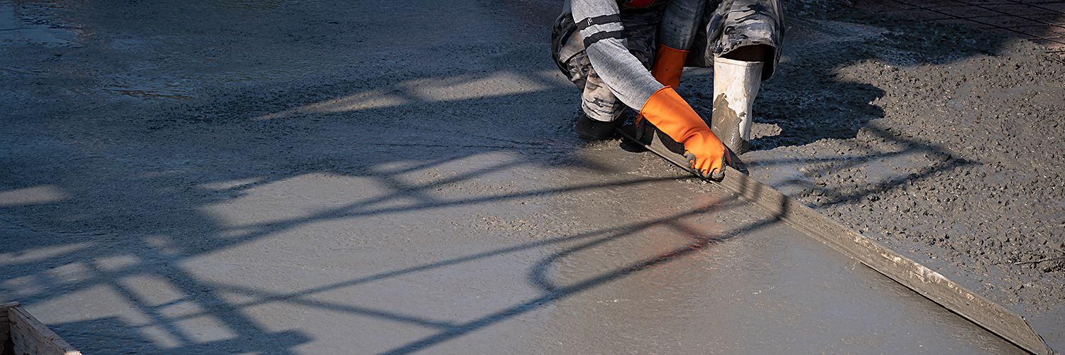 Cropped image of Asian construction worker using long triangle trowel to plastering cement on the floor in construction site